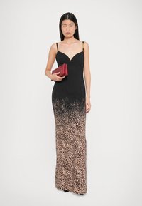 Robe maxi noire avec un dégradé imprimé léopard, comportant des fines bretelles et des accents en métal doré. Le mannequin tient une pochette rouge.