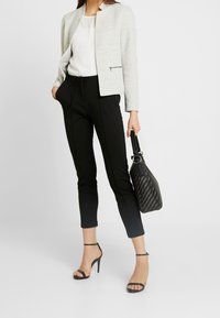 Blazer gris clair sur un haut blanc, associé à un pantalon noir fuselé et des talons noirs à brides. Porte un sac à main noir texturé.
