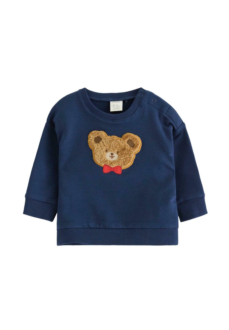 Granatowy niemowlęcy sweter z prążkowanymi mankietami, z futrzanym naszywką w kształcie twarzy misia, który ma na sobie czerwoną muszkę z przodu.