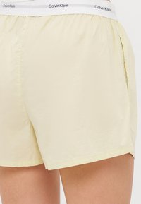 Lichtgele shorts gemaakt van zachte stof, met een elastische tailleband en een wit Calvin Klein-logo. Inclusief zijzakken.