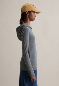 Grijze hoodie met een gestructureerde afwerking en een capuchon met trekkoord, gecombineerd met een gele pet. Het ontwerp heeft lange mouwen en een aansluitende pasvorm.