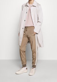 Chubasquero gris claro sobre un suéter rosa y pantalones jogger beige con rayas laterales, combinados con zapatillas blancas. Texturas suaves y ajuste relajado.