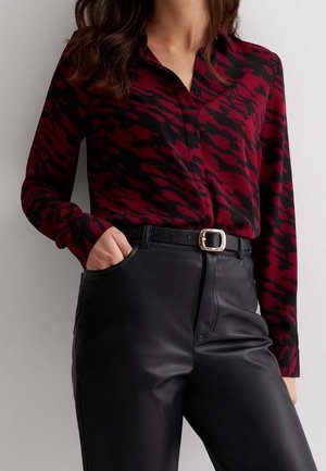 Rode en zwarte blouse met patroon, gemaakt van gladde stof, met kraag en knoopsluiting aan de voorkant, gecombineerd met zwarte leren broek met hoge taille en een riem.