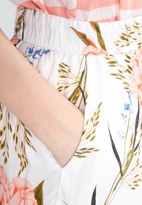 Blommönstrad tyg med vit bakgrund; har resårmidja och sidficka. Mönstret inkluderar rosa blommor och gröna blad.