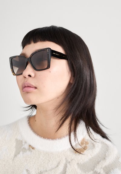 Lunettes de soleil avec des montures carrées surdimensionnées en écaille foncée avec des verres dégradés marron ; comportent de petits points d'accent sur la monture.