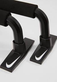 Mustat paralletit treenaukseen, joissa on tekstuurilla varustetut vaahtogriipit, kaarevat metallirangat ja kahdeksankulmaiset pohjat, joissa on valkoiset Nike-swoosh-logot.