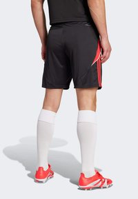 Sorte atletiske shorts med røde accenter, parret med hvide knælange sokker og lyse røde fodboldstøvler, med en glat overflade og tætsiddende design.