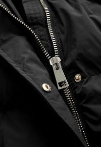 Schwarze wasserdichte Jacke mit einem silbernen Reißverschluss mit großem Zipper, dezentem Muster und einem Druckknopf-Akzent.