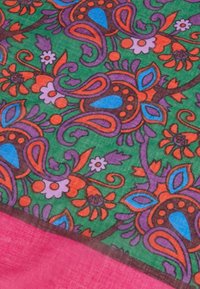 Kleurrijke stof met een groen achtergrond en bloemen- en paisleymotieven in paars, oranje en blauw, omrand met een roze rand.