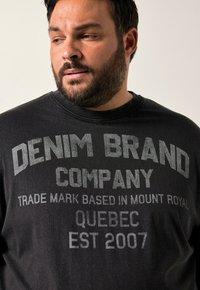 Schwarzer Baumwoll-Sweatshirt mit Rundhalsausschnitt, auffälligem grauem Text: "DENIM BRAND COMPANY TRADE MARK BASED IN MOUNT ROYAL QUEBEC EST 2007."