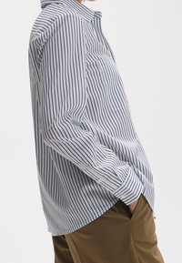 Gestreiftes Hemd in Weiß und Marineblau, mit Kragen, langen Ärmeln und einer Brusttasche. Der Stoff hat eine glatte Oberfläche und einen lässigen Schnitt.