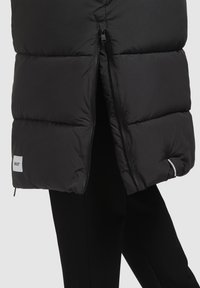 Sort puffersjakke med en quiltet design, der har lynlås foran og logoetiket. Glat tekstur og kort længde med sidelommer.