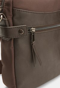 Brown textured leather shoulder bag with a smooth bottom section, accented by a zipper and a fabric panel above. Features adjustable strap.