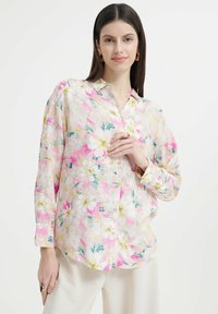 Langarm-Hemd mit Knöpfen aus leichtem Stoff, mit einem floralen Muster in Rosa-, Weiß- und Grüntönen auf einem hellen Hintergrund.
