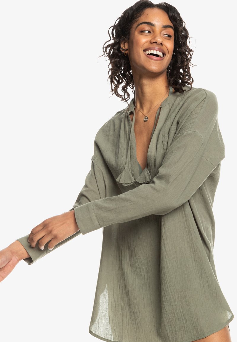 Blusa di colore verde oliva, ampia e comoda in un tessuto leggero e texturizzato, con scollatura a V profonda e maniche lunghe. Presenta un delicato dettaglio plissettato.