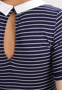 Mörkblå skjorta med vita horisontella ränder, vit krage och djup nyckelhålsöppning fram som visar huden under.