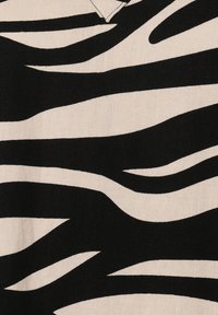 Stoff in Schwarz und Creme mit einem Zebra-Streifenmuster. Die Textur scheint gewebt zu sein, mit unterschiedlich breiten Streifen.