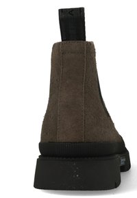 Bruine suède enkelboot met een textuurafwerking, zwarte rubberen zool en een zwarte trekflap aan de achterkant voor gemakkelijk aan- en uittrekken.