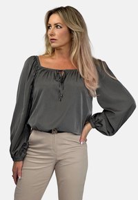 Szara bluzka z długim rękawem, o kwadratowym dekolcie, z wiązaniem na sznurki i rękawami balonowymi, zestawiona z beżowymi dopasowanymi spodniami. Gładka faktura.