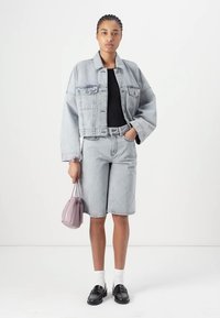Ljust grå denimjacka med en kortad modell, i kombination med matchande shorts. Svart topp, vita strumpor och svarta skor. Håller en liten lila väska.