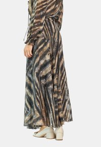 Fließender Maxirock aus transparenter Stoff mit braunem und grauem Wellenmuster, mit einem gerafften Bund und langen Ärmeln, kombiniert mit weißen Blockabsatzschuhen.