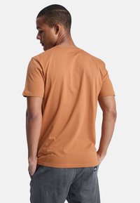 Kurzärmeliges T-Shirt mit Rundhalsausschnitt in Rostorange. Hergestellt aus weicher Baumwolle, mit lässigem Schnitt und glatter Textur. Einfaches Design, keine Grafik.