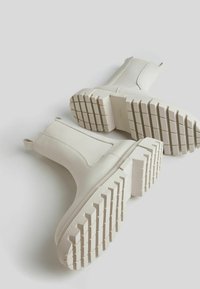 White ankle boots with a smooth, matte finish; elastic side panels; textured sole with prominent treads; pull tabs for easy wear.