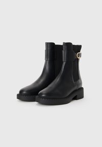 Bottines en cuir noir avec un bout arrondi, des panneaux latéraux élastiques et une sangle décorative avec des éléments en or. Semelle épaisse pour plus de stabilité.