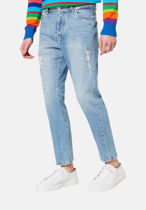 Persona che indossa jeans chiari strappati, sneakers bianche e un maglione a righe colorate con righe blu, rosse, verdi e arancioni.