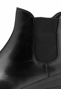 Bottines Chelsea en cuir noir avec panneaux latéraux en élastique et finition lisse et polie, mettant en avant un gros plan de la zone de la cheville.