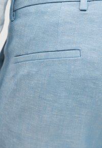 Υφασμα σε ανοιχτό μπλε χρώμα με κοντινή εικόνα μιας οριζόντιας πίσω τσέπης και λεπτομέρειες από τη μέση.