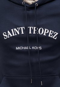 Sweat à capuche bleu marine avec cordons blancs, avec un texte brodé blanc "SAINT TROPEZ" et un plus petit "MICHAEL KORS" en dessous.