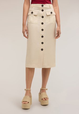 Beige midi-rok met knopen aan de voorkant en grote klepzakken, gedragen met beige platformsandalen en een rood topje.