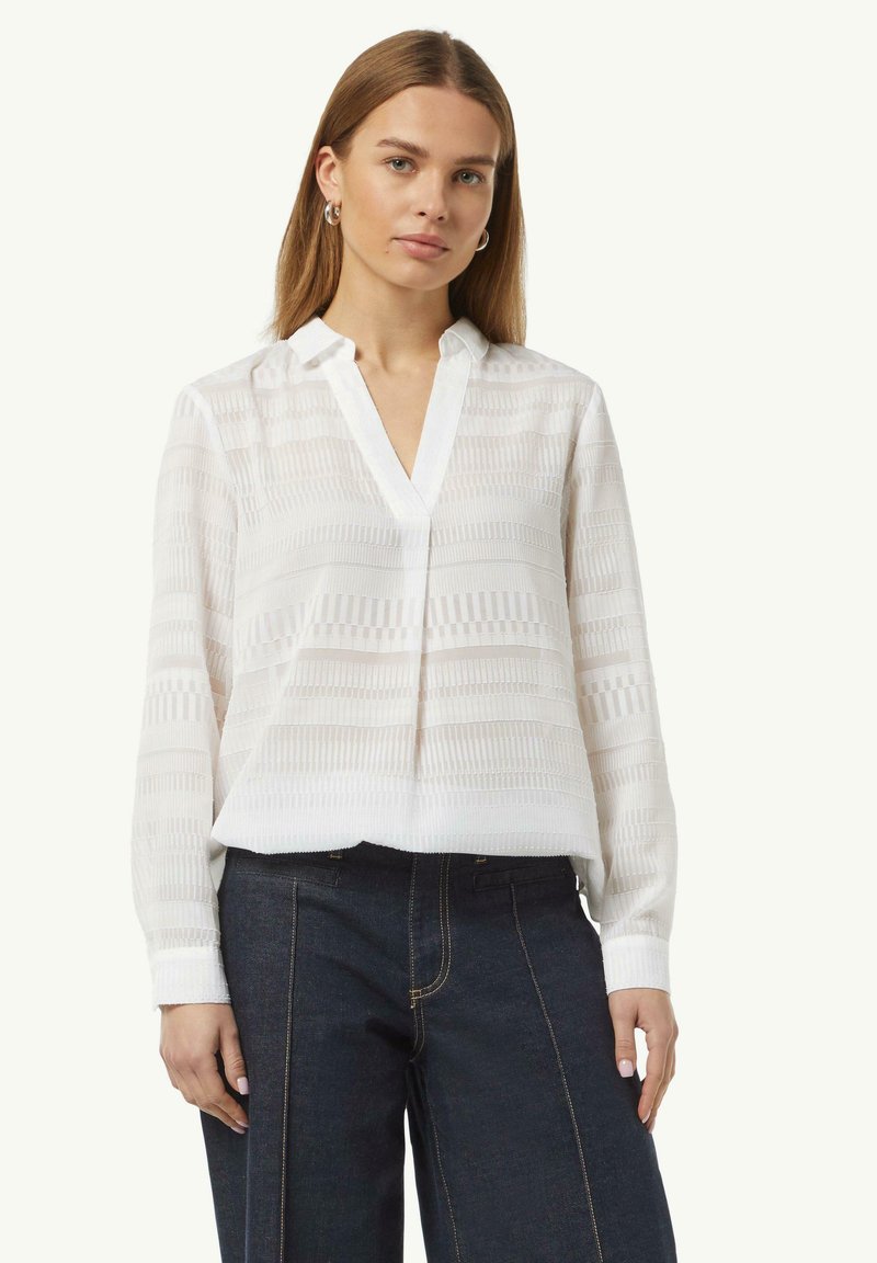 Weiße Bluse mit langen Ärmeln, Kragen und strukturiertem Streifenmuster. Kombiniert mit dunklen Jeans. Glattes Material, lockere Passform.