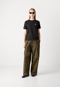 T-shirt in cotone nero con grafica piccola, abbinato a pantaloni a palazzo con stampa leopardata in tonalità terrose. Modella che indossa occhiali da sole neri e eleganti.