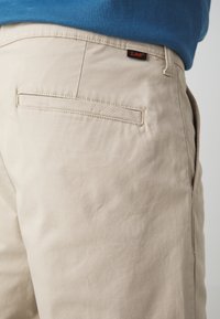 Beige Hosen aus Baumwolle mit einer glatten Textur. Verfügt über eine Gesäßtasche mit Nähdetail und einem kleinen schwarzen und orangenen Lee-Tag.