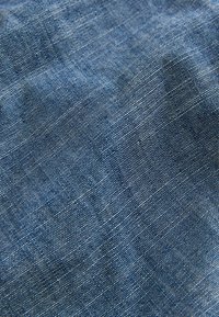Tessuto blu intrecciato con una superficie texturizzata, caratterizzato da un motivo screziato di fili più chiari, che mostra un aspetto morbido e naturale.