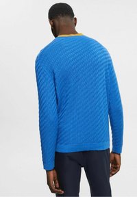 Modrý svetr s texturou a diamantovým vzorem, s dlouhými rukávy a žlutým límcem. Ribbenkované manžety a lem dotvářejí design.