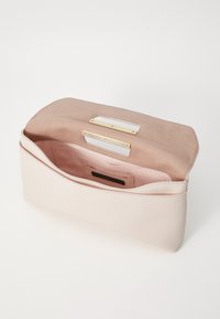Vaaleanpunainen clutch-laukku, joka on valmistettu sileästä nahasta ja jossa on mokkinen sisustus. Laukussa on vetoketj pocket ja kaksi kultasävyistä varustetta.