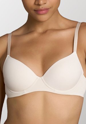 Reggiseno imbottito beige con coppe lisce, spalline sottili e regolabili, e design senza cuciture. Presenta una fascia di supporto a forma di U.