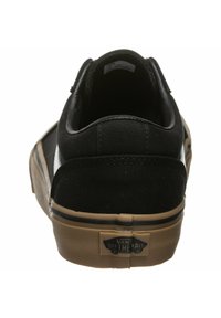 Zapatilla de lona negra con punta redonda y talón reforzado. Presenta una suela de goma marrón y una etiqueta de logo blanca en el talón.