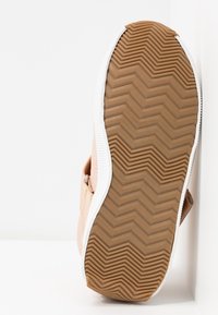 Chaussure avec une tige synthétique couleur fauve, des détails blancs, et une semelle extérieure en caoutchouc brun texturée présentant un motif de bande de roulement en zigzag pour une meilleure adhérence.