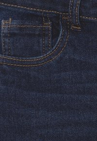 Tejido de denim azul oscuro con costuras naranjas visibles que delinean un pequeño bolsillo para monedas y parte de un bolsillo delantero.