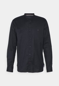 Czarna koszula z długim rękawem, z kołnierzykiem mandaryńskim, z zapięciem na guziki i subtelnym detalem logo. Wykonana z gładkiego materiału o regularnym kroju.