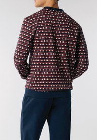 Uomo che indossa un maglione a maniche lunghe, con un motivo a strisce rosse e blu navy e piccole forme bianche, abbinato a pantaloni blu navy, girato di spalle.