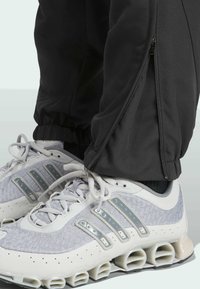 Black athletic pants with side zippers and elastic cuffs, paired with gray and white mesh sneakers featuring distinctive plastic accents.