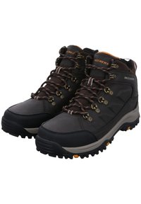 Botas de senderismo negras con acentos marrones, que cuentan con un tejido duradero, ojetes de metal, suelas texturizadas y detalles naranjas en la parte inferior.
