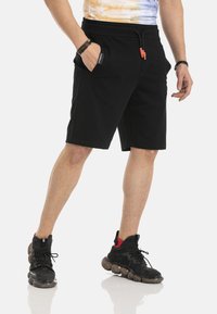 Zwarte katoenen shorts met een elastische tailleband en trekkoord, voorzien van zijzakken. Gecombineerd met zwart-rode sportschoenen.