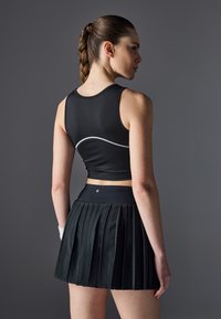 Crop top sportiv negru cu cusături albe, combinat cu o fustă plisată neagră cu o talie lată. Material neted, ajustat.