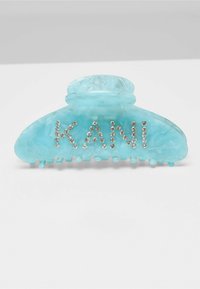 A large turquoise hair clip made of glossy plastic, featuring the word "KANI" adorned with clear rhinestones. Textured grip teeth at the bottom.